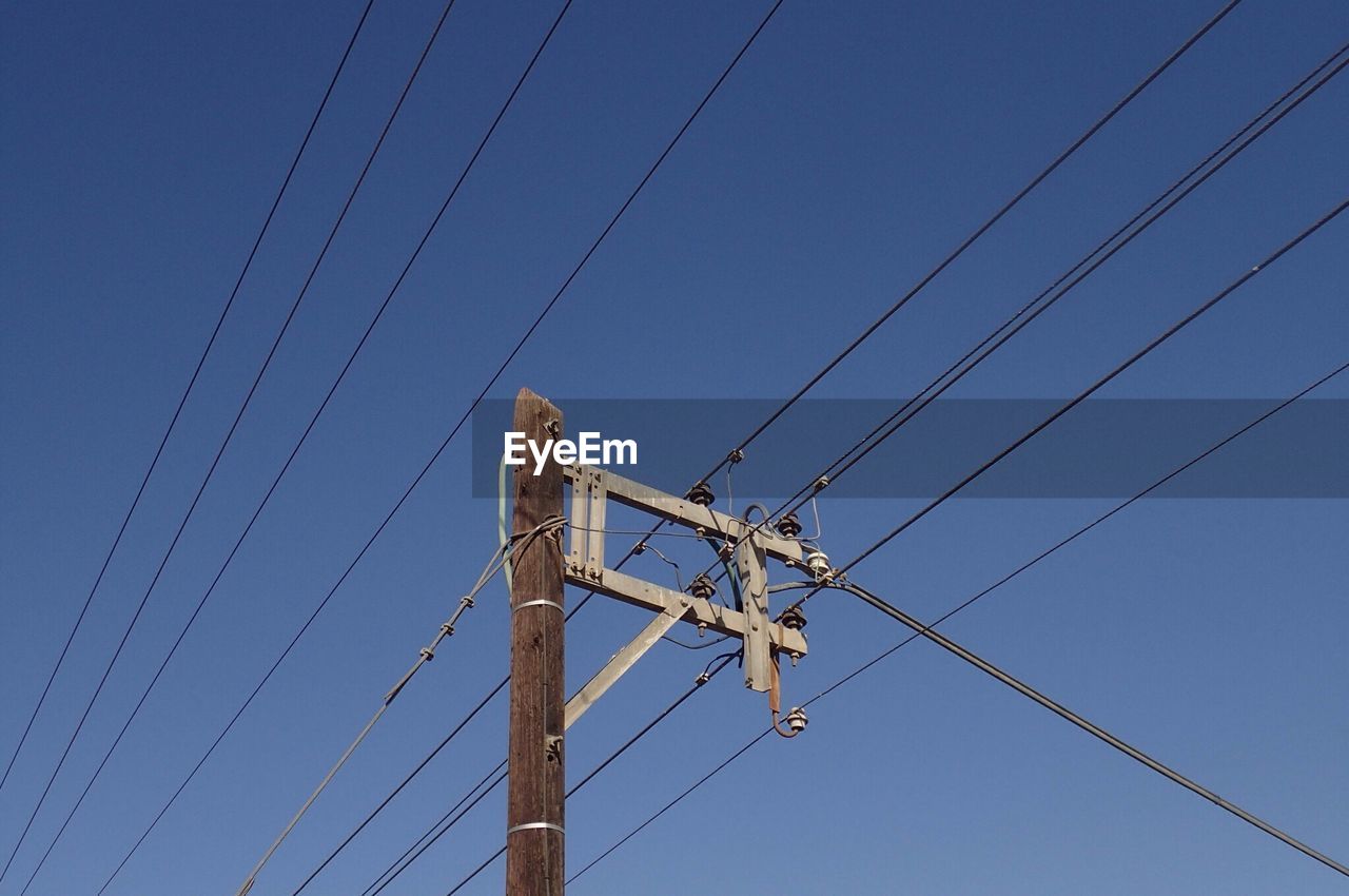 Low angle view of electricity pylon against clear blue sky