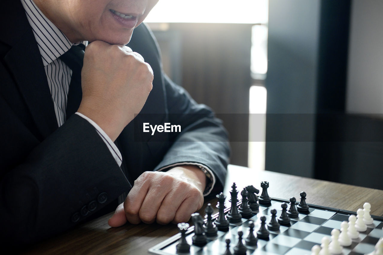 Midsection of businessman playing chess at table in office