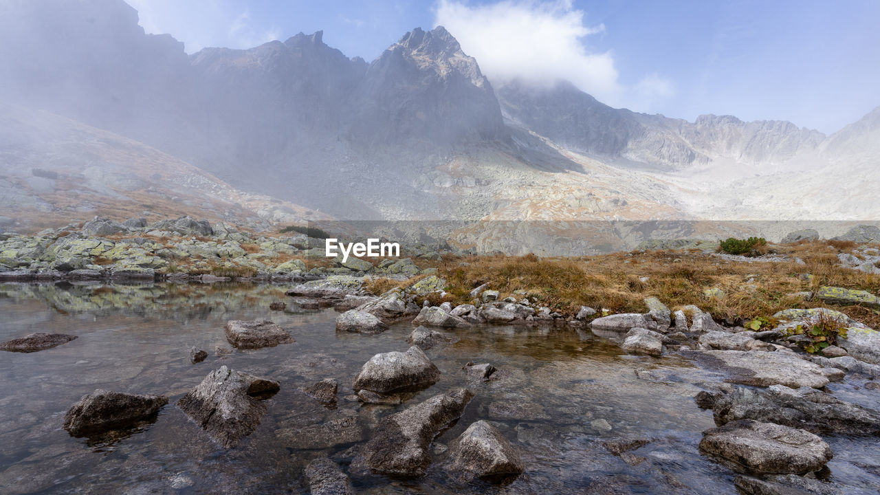 mountain, wilderness, landscape, environment, scenics - nature, beauty in nature, nature, mountain range, sky, rock, land, valley, travel, cloud, water, fog, travel destinations, geology, no people, outdoors, plateau, adventure, ridge, cold temperature, tourism, non-urban scene, snow, mountain peak, tranquility, lake, day, activity, walking, tranquil scene, panoramic, plant