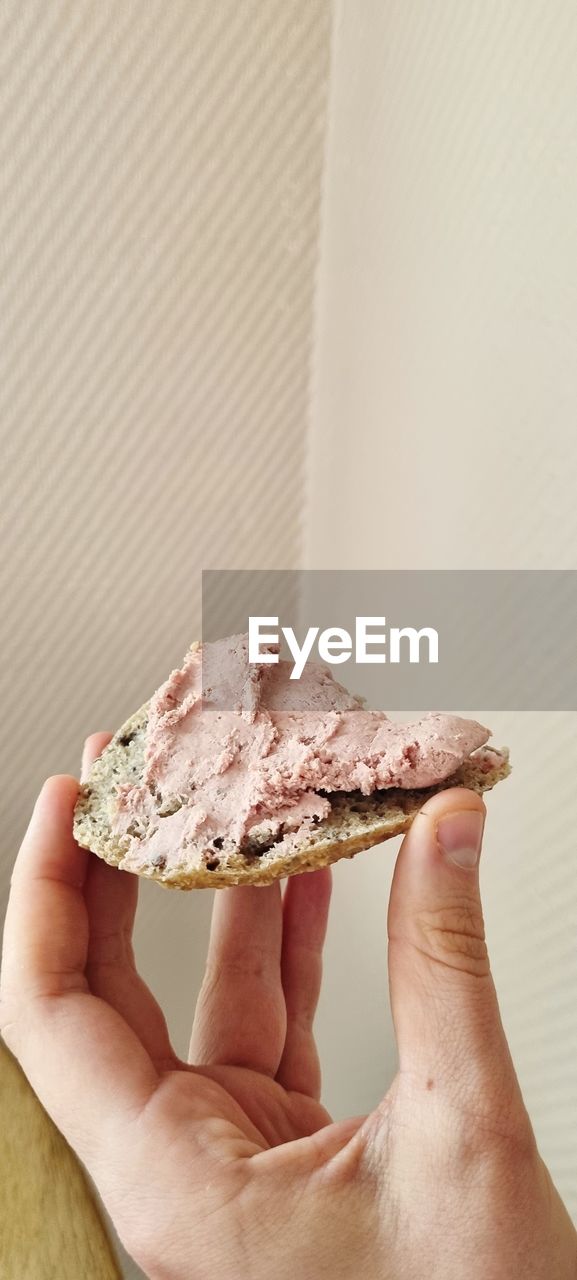 CLOSE-UP OF HAND HOLDING BREAD AGAINST WALL