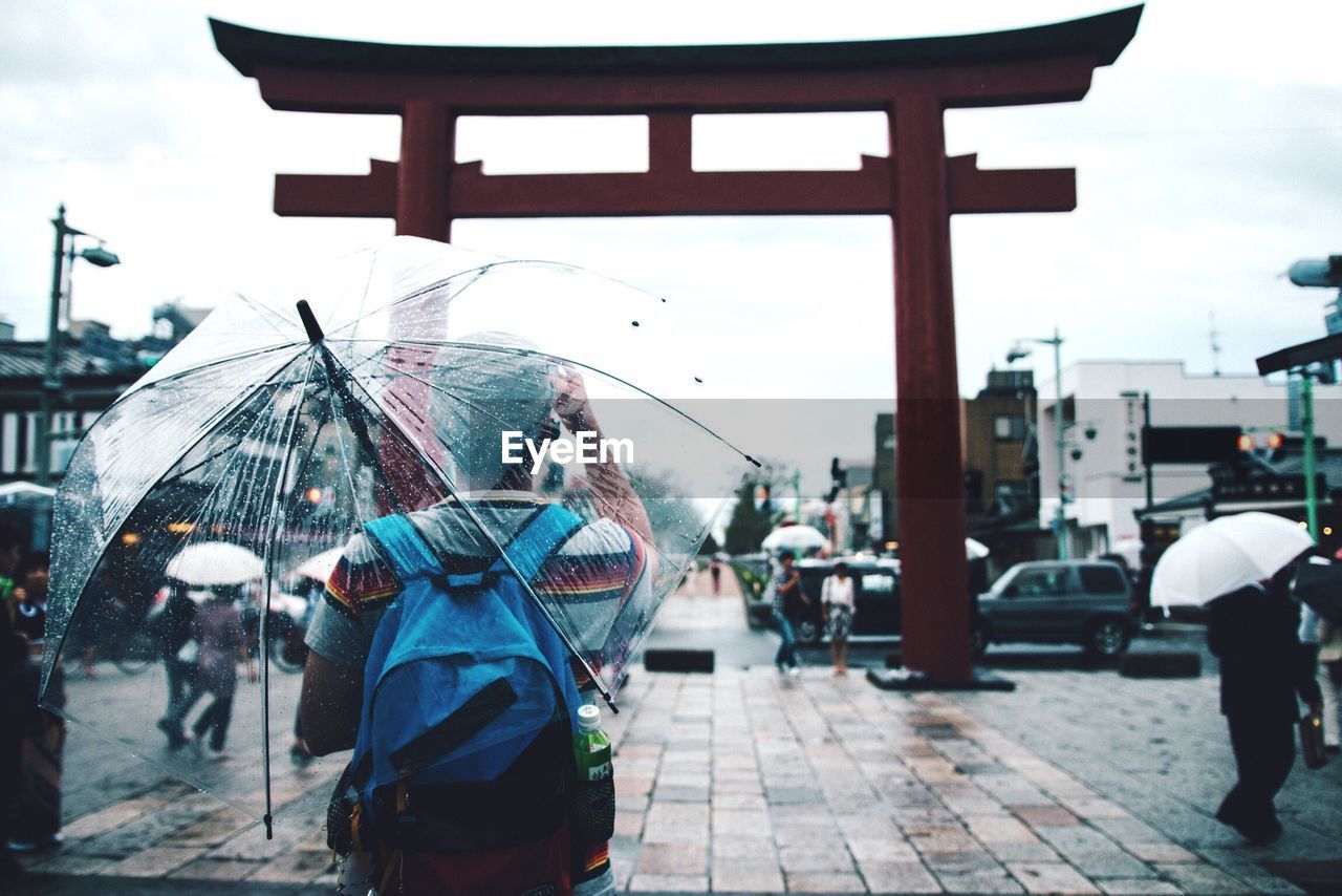 Rear view of tourist standing with umbrella by torii gate during rain