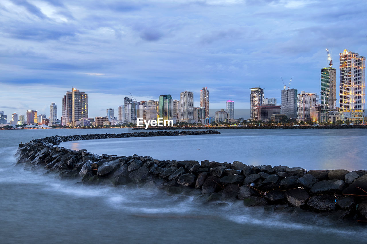 Buildings by sea in city against sky during dusk