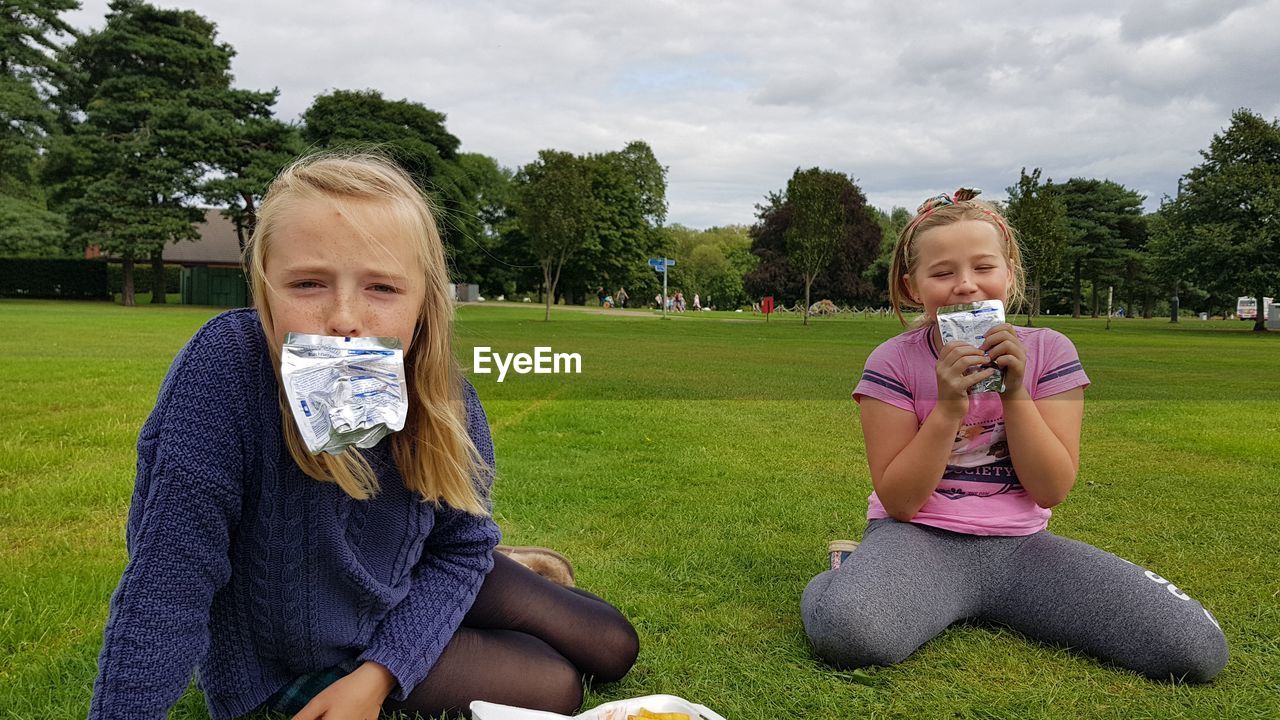 Portrait of girls sitting with food packages on grass at park