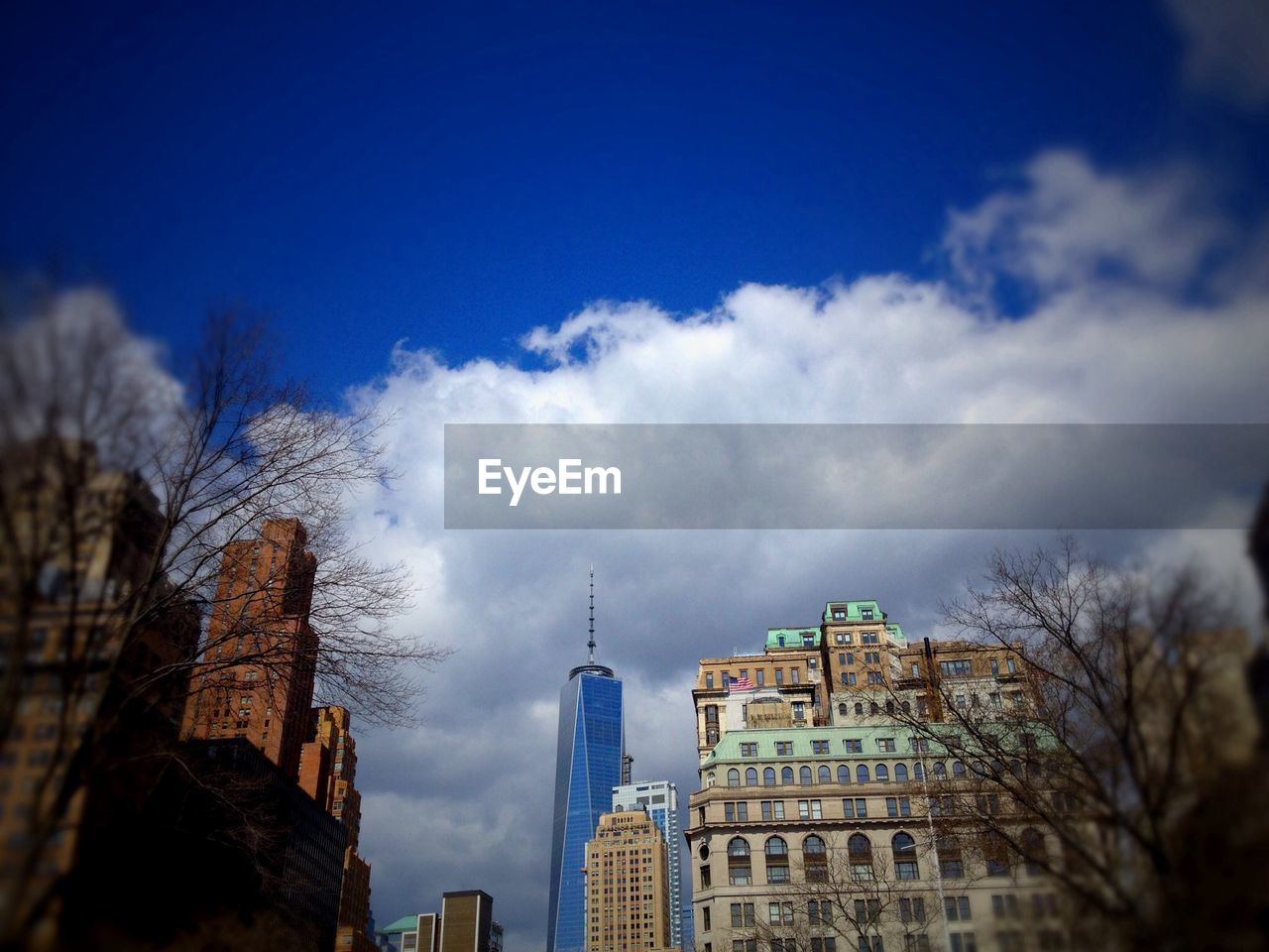 Low angle view of one world trade center amidst buildings against cloudy sky