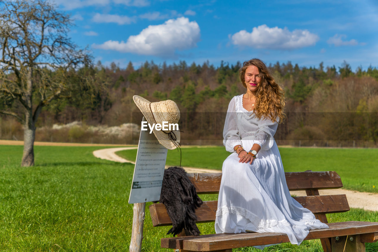 Portrait of smiling woman sitting on bench against trees