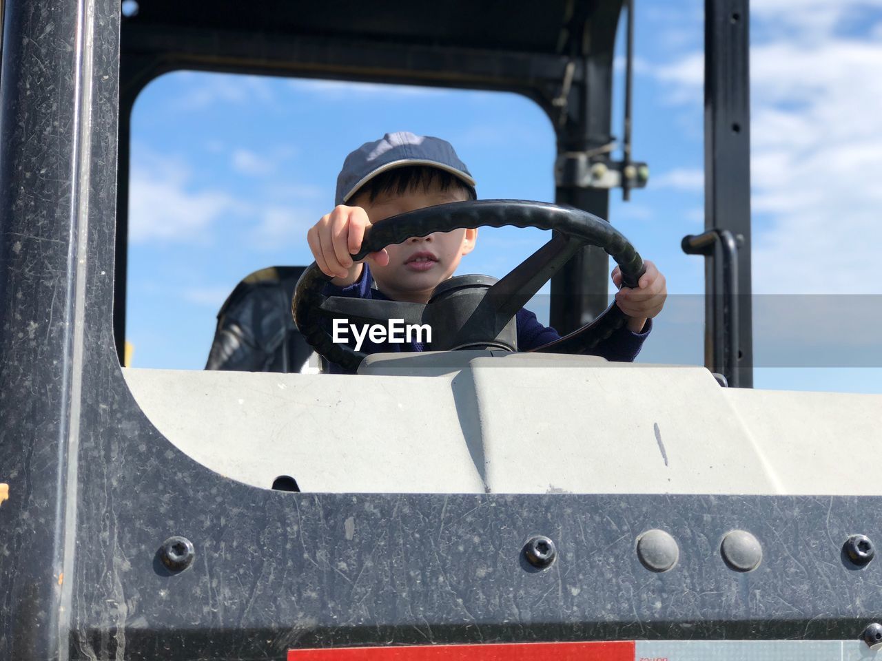 Low angle view of boy holding steering wheel of vehicle against sky