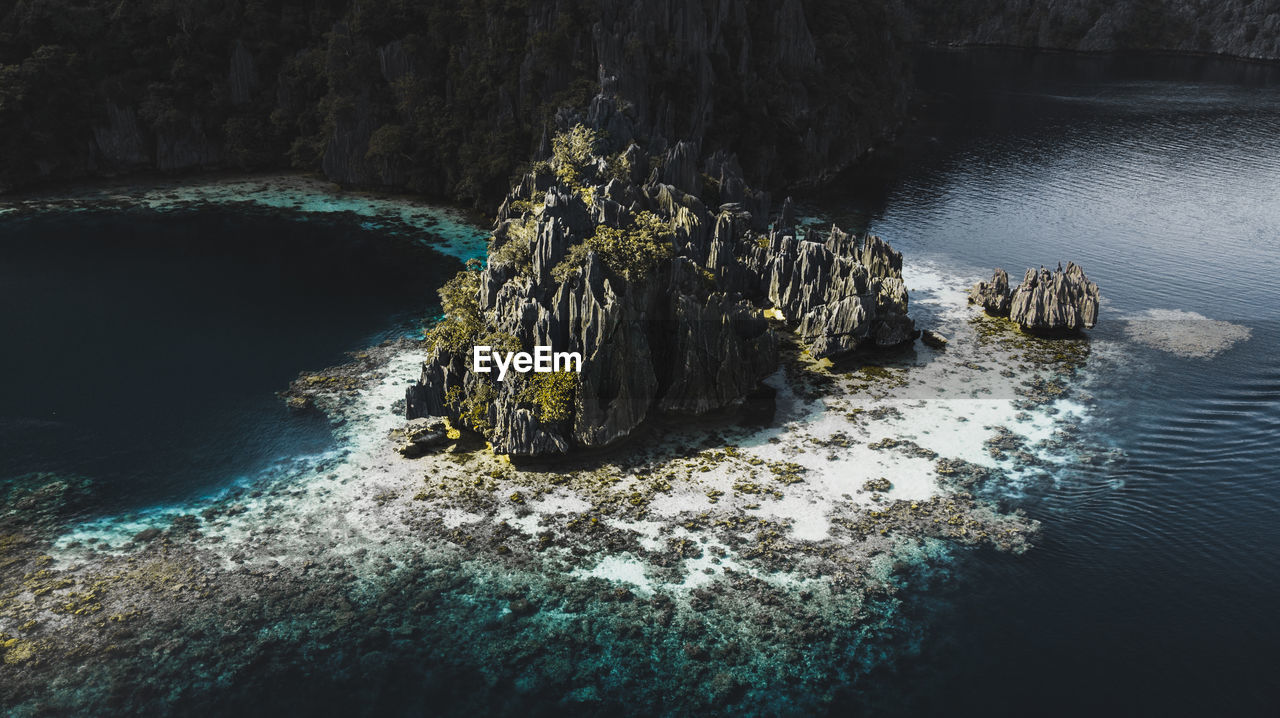 Aerial view of rough rocks on island with green plants among blue calm sea in coron, philippines