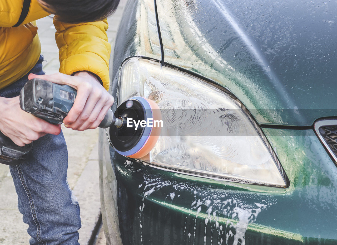 The hands of a guy are drilling with a sponge and polishing the headlight