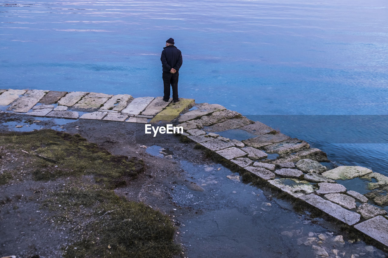 REAR VIEW OF MAN STANDING AT SHORE