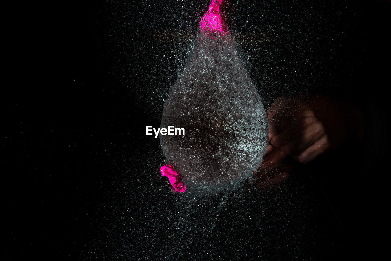 Close-up of pink water balloon bursting against black background