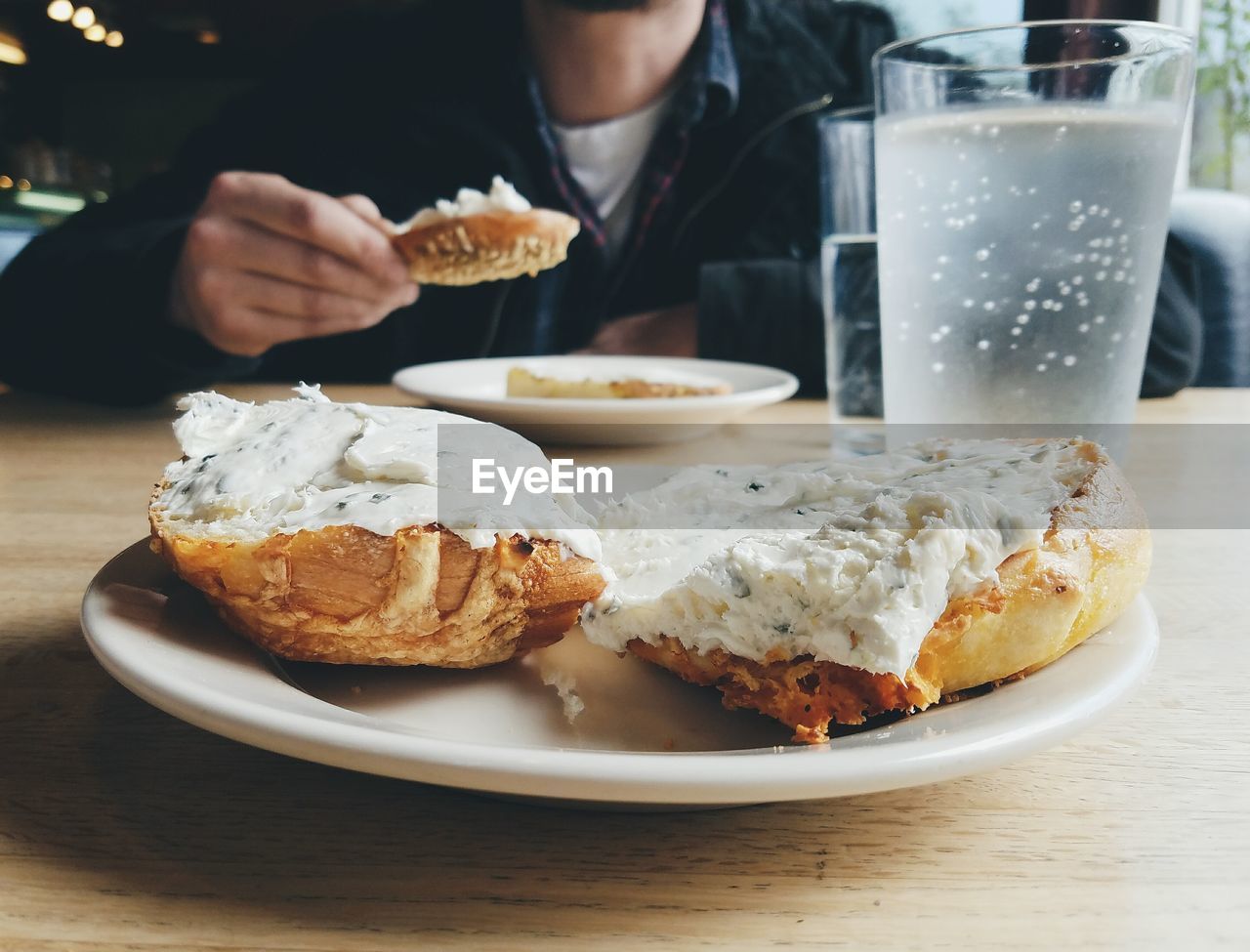 Midsection of person having cream cheese bagel at restaurant