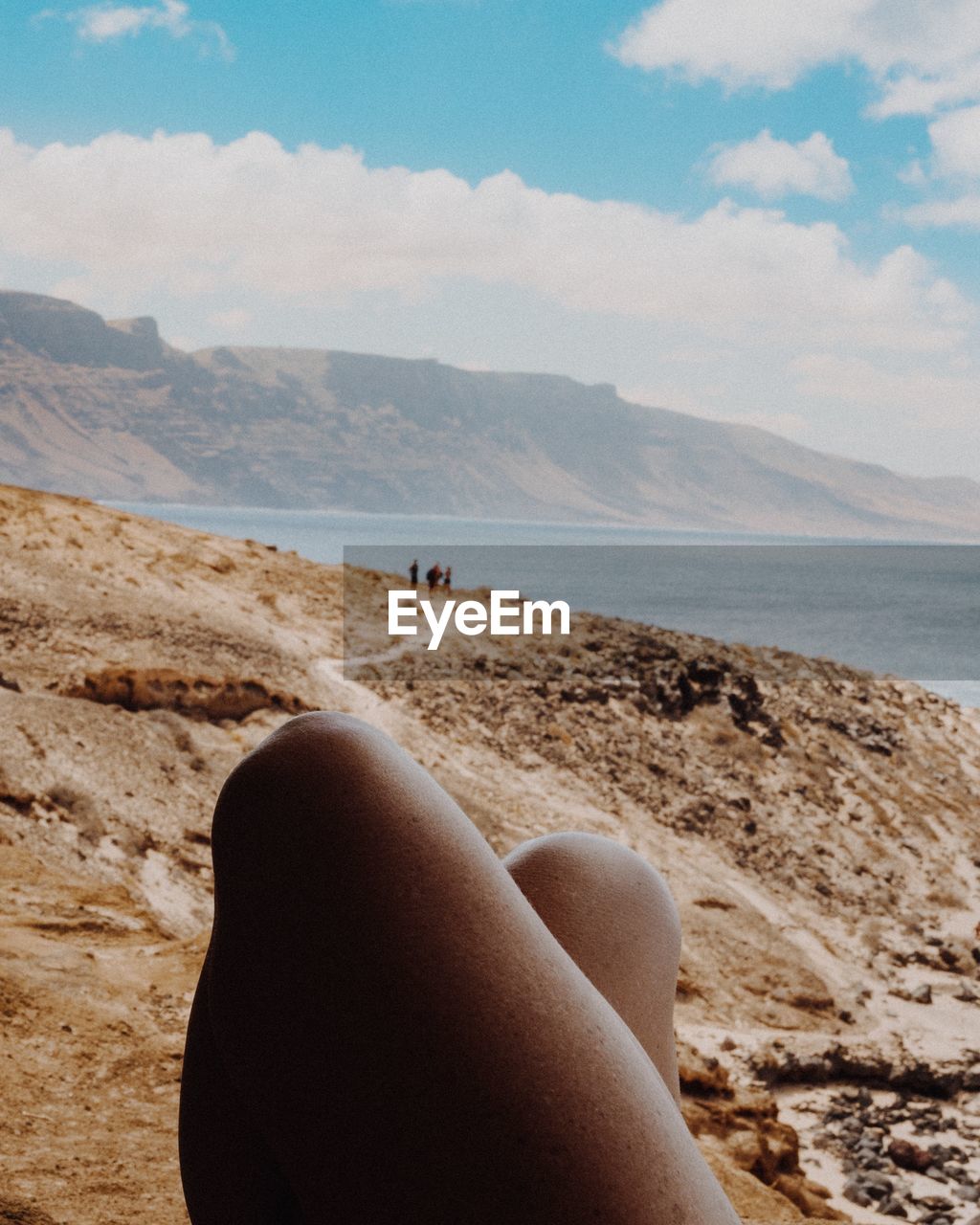 Low section of person relaxing on beach against sky