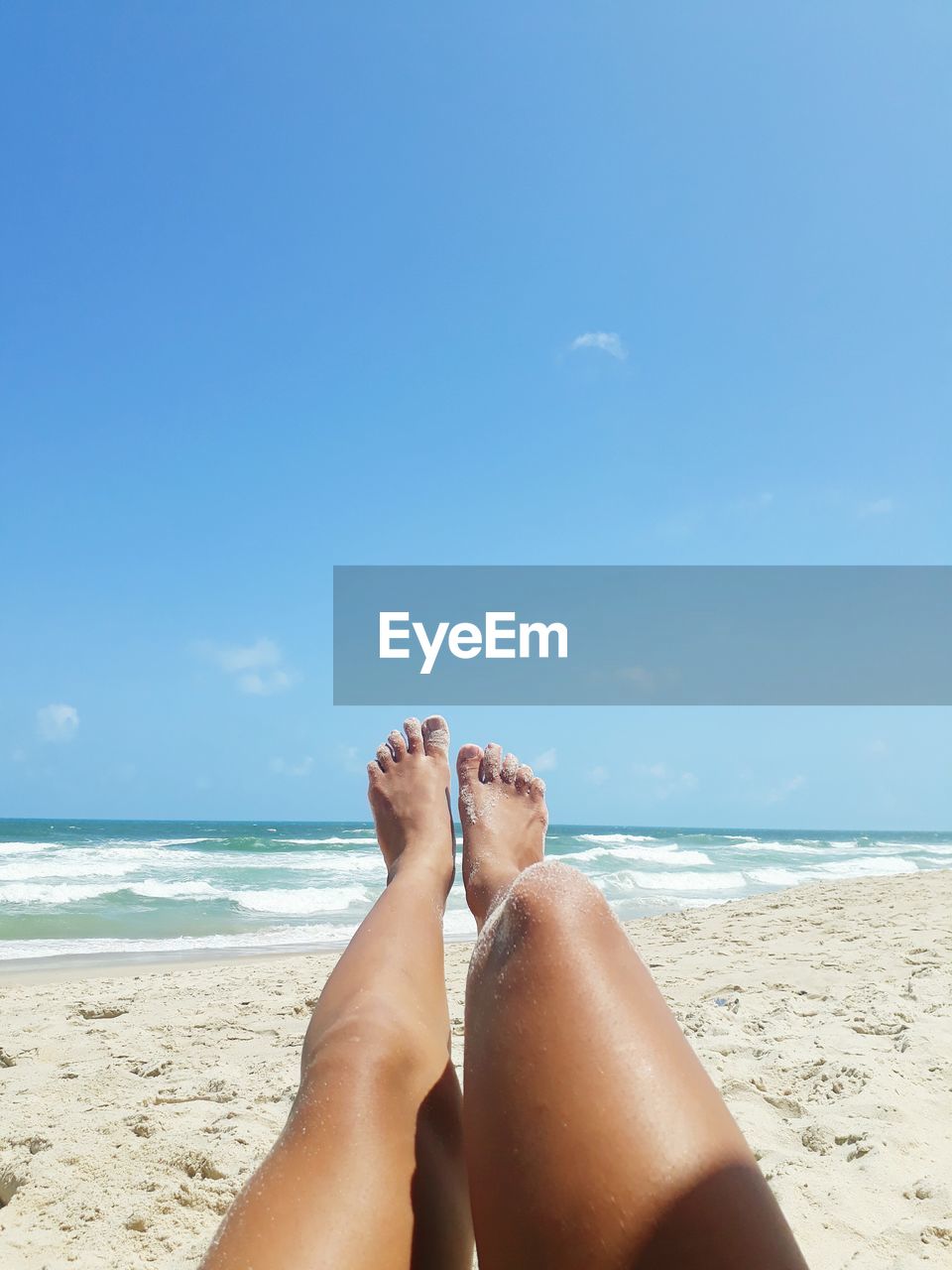 Low section of woman legs on beach against blue sky