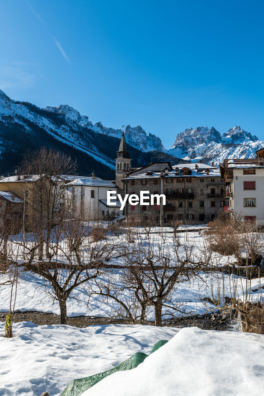 SNOW COVERED BUILDINGS BY MOUNTAINS AGAINST SKY