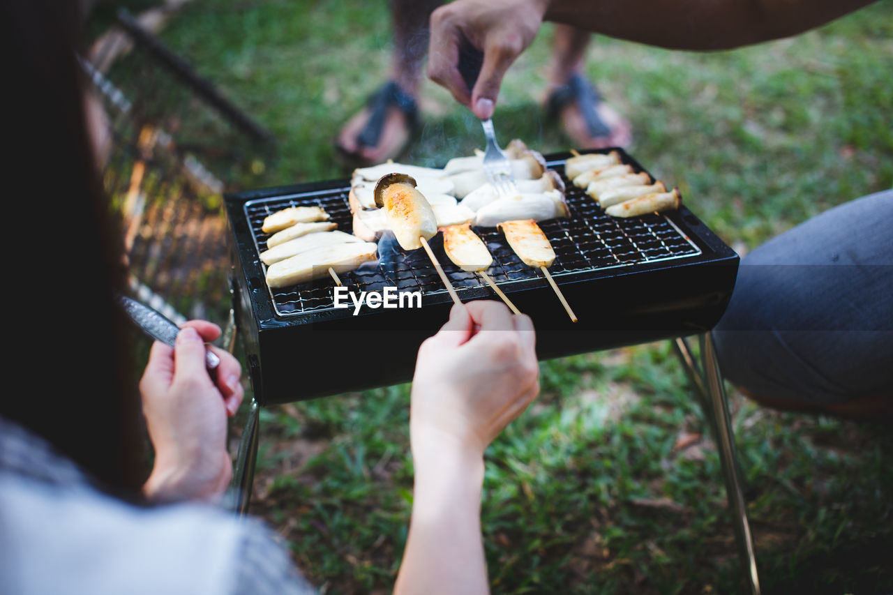 Close-up of people preparing food on barbecue grill in yard