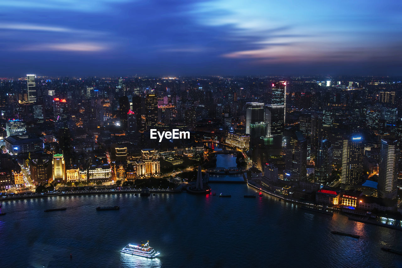 Aerial view of illuminated buildings by river in city at night