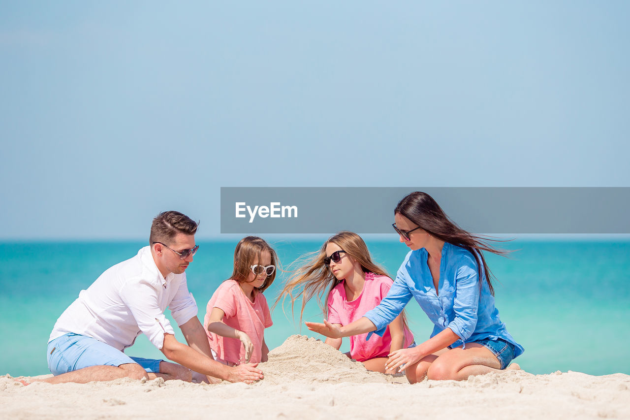 WOMEN SITTING ON BEACH AGAINST CLEAR SKY