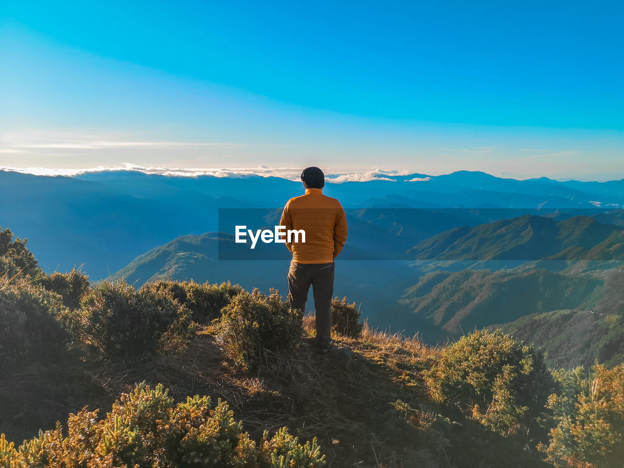 REAR VIEW OF MAN LOOKING AT MOUNTAINS