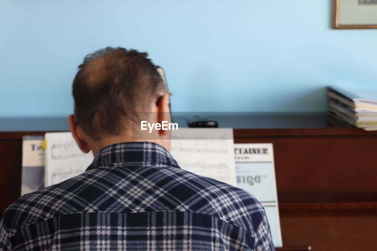 REAR VIEW OF MAN SITTING BY TABLE AT HOME