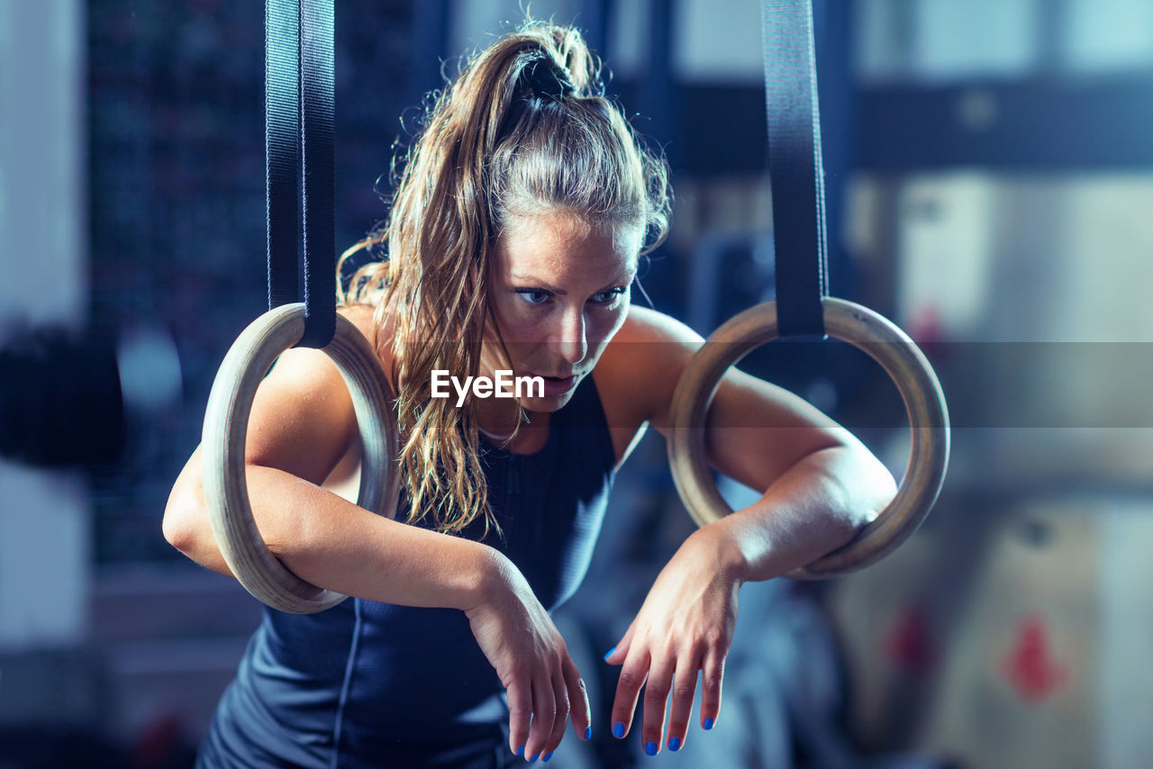 Tired female athlete exercising with gymnastic rings in gym