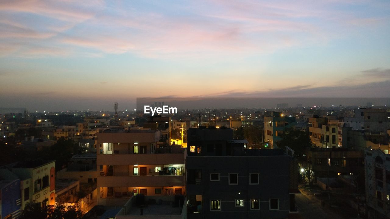 Illuminated cityscape against sky at sunset