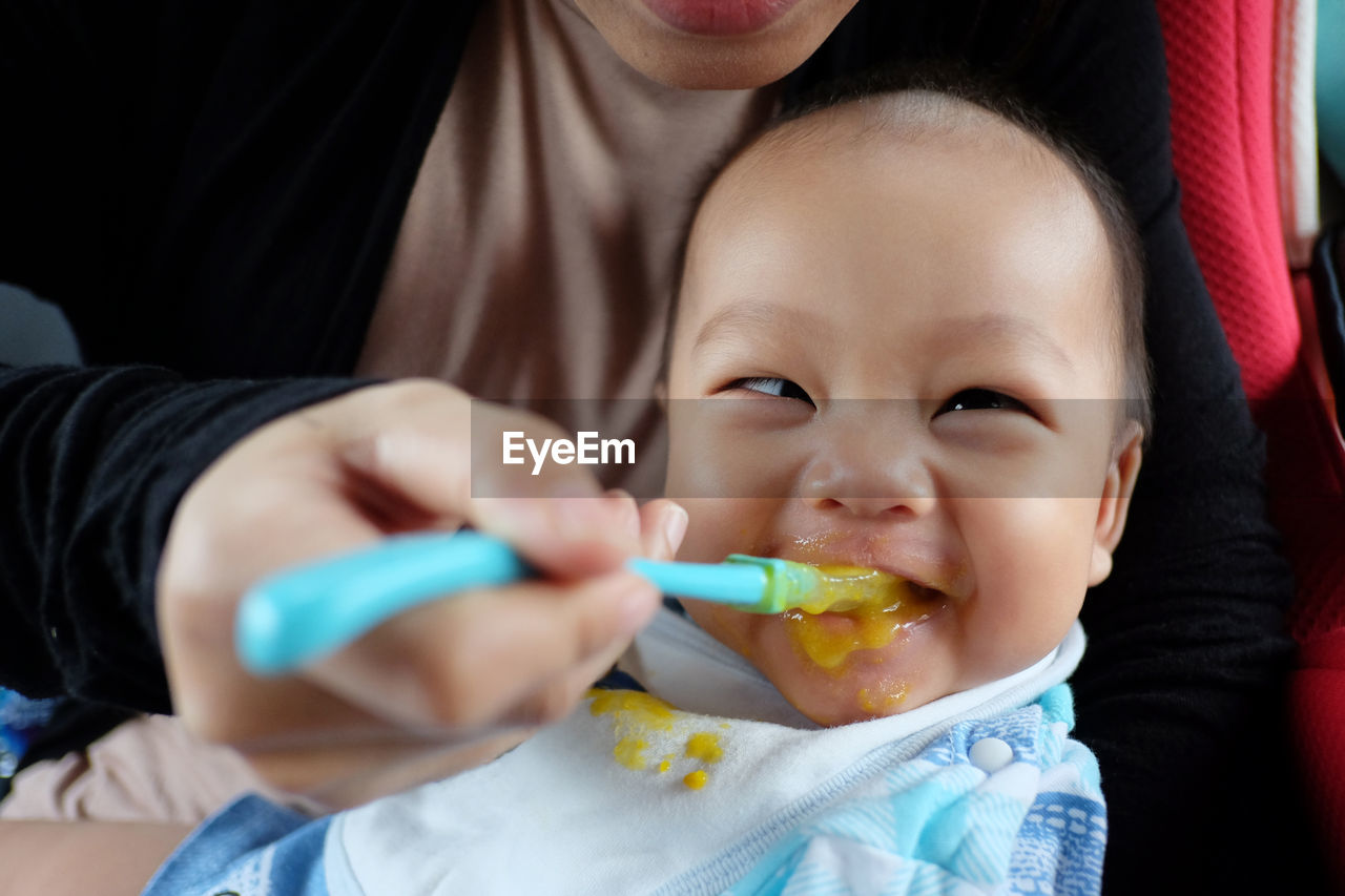 Midsection of mother feeding baby at home