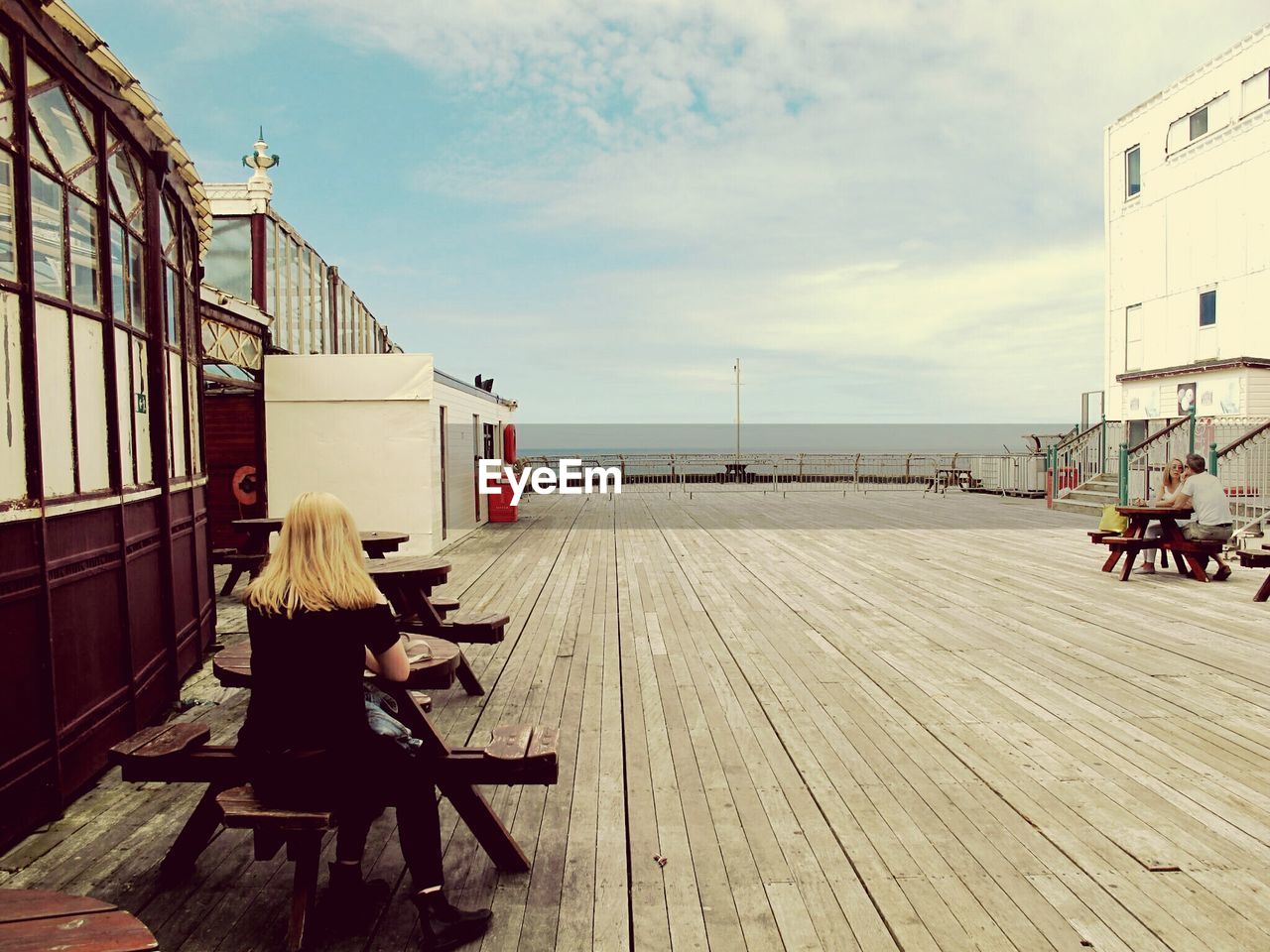 People sitting at table on north pier against cloudy sky