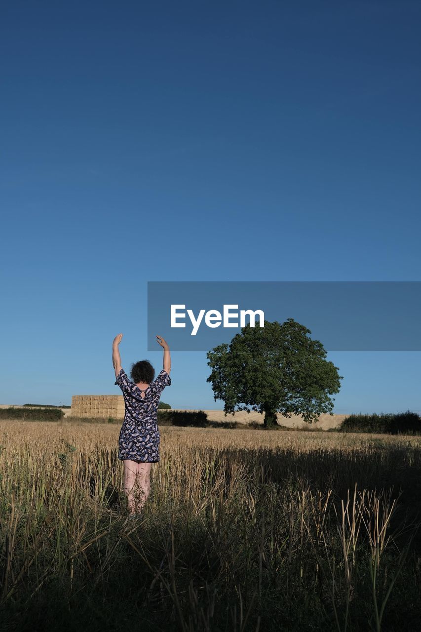 Rear view of woman standing with arms raised on land against clear sky