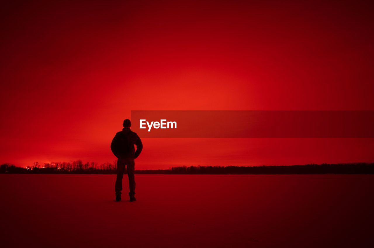 SILHOUETTE OF MAN STANDING ON RED LANDSCAPE AGAINST SKY