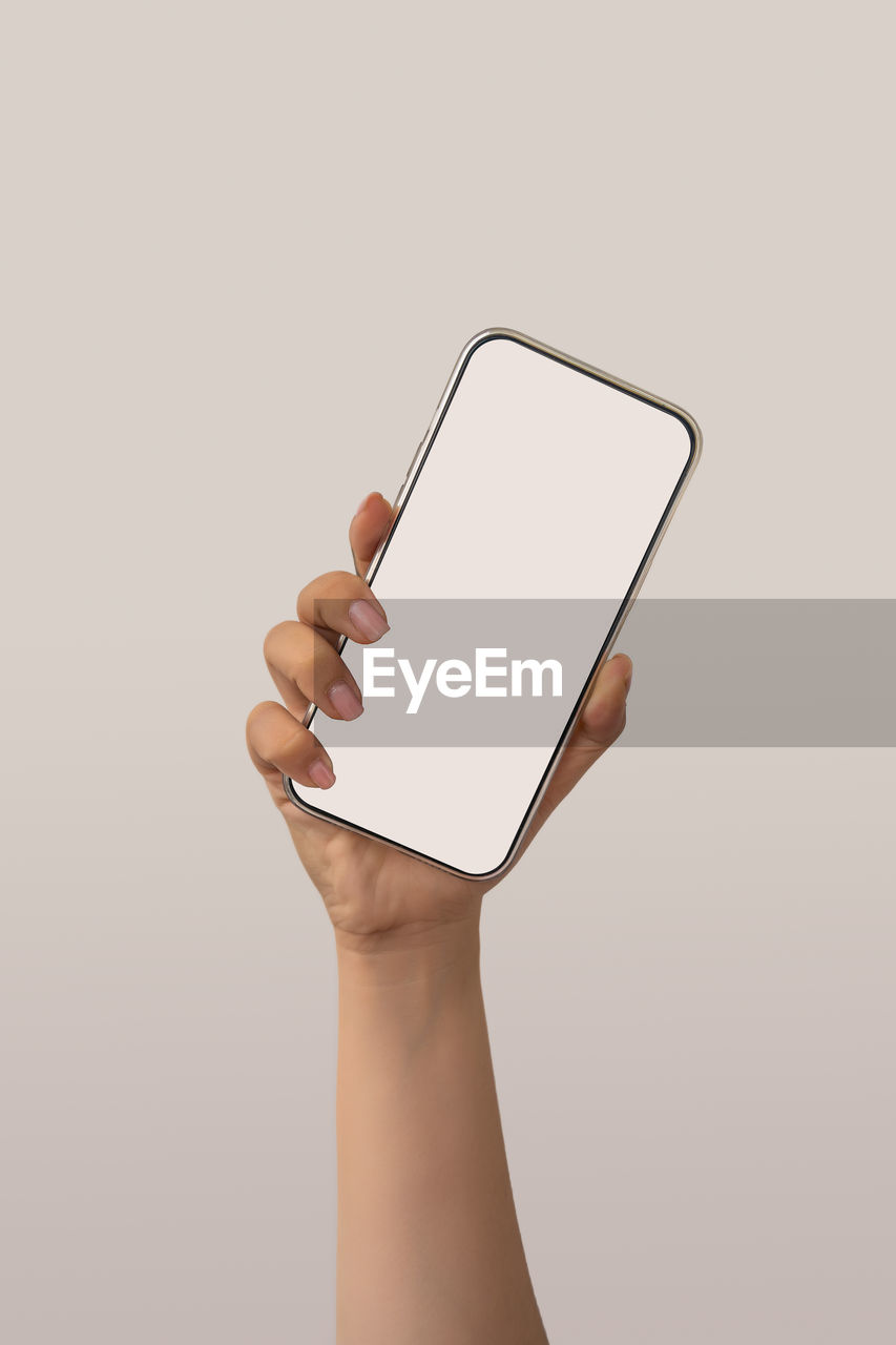 CLOSE-UP OF HAND HOLDING MOBILE PHONE AGAINST WHITE BACKGROUND