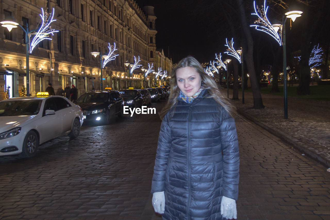 Portrait of young woman standing on street at night