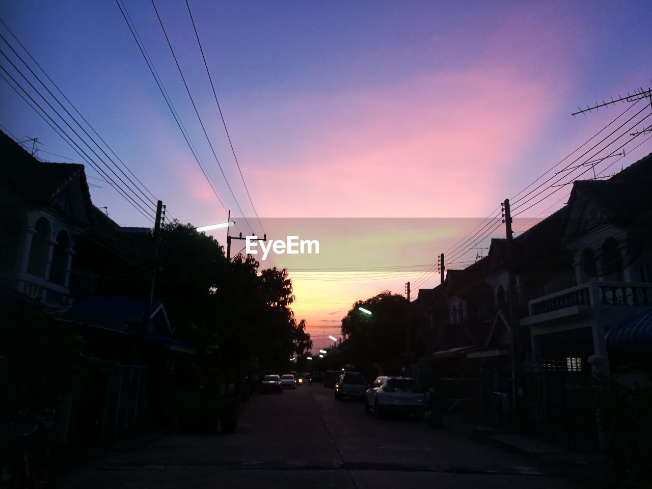 CARS ON ROAD AMIDST BUILDINGS AGAINST SKY DURING SUNSET