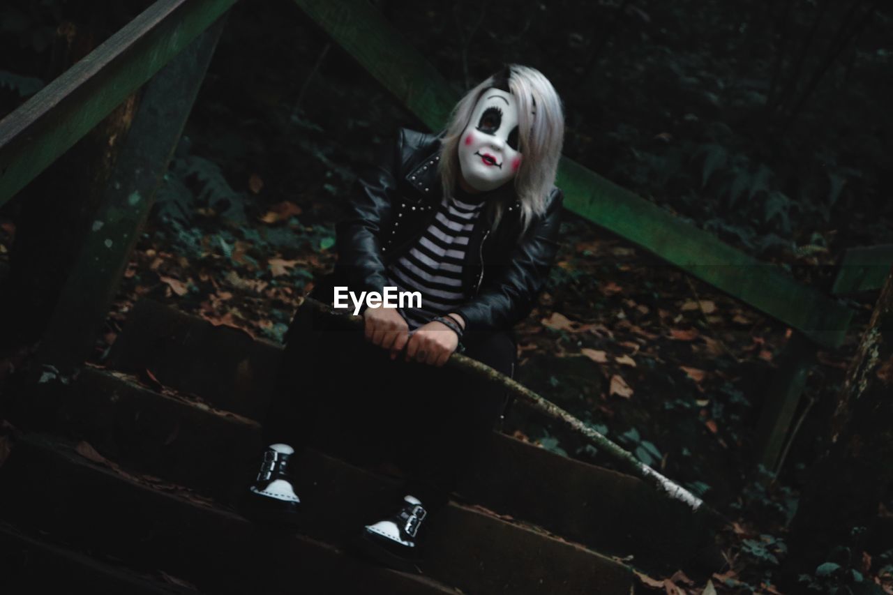 Portrait of man wearing mask while sitting on steps in forest