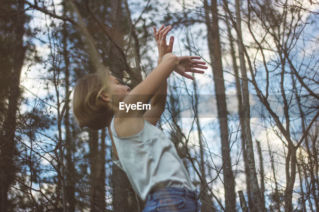 Low angle view of young woman dancing in forest