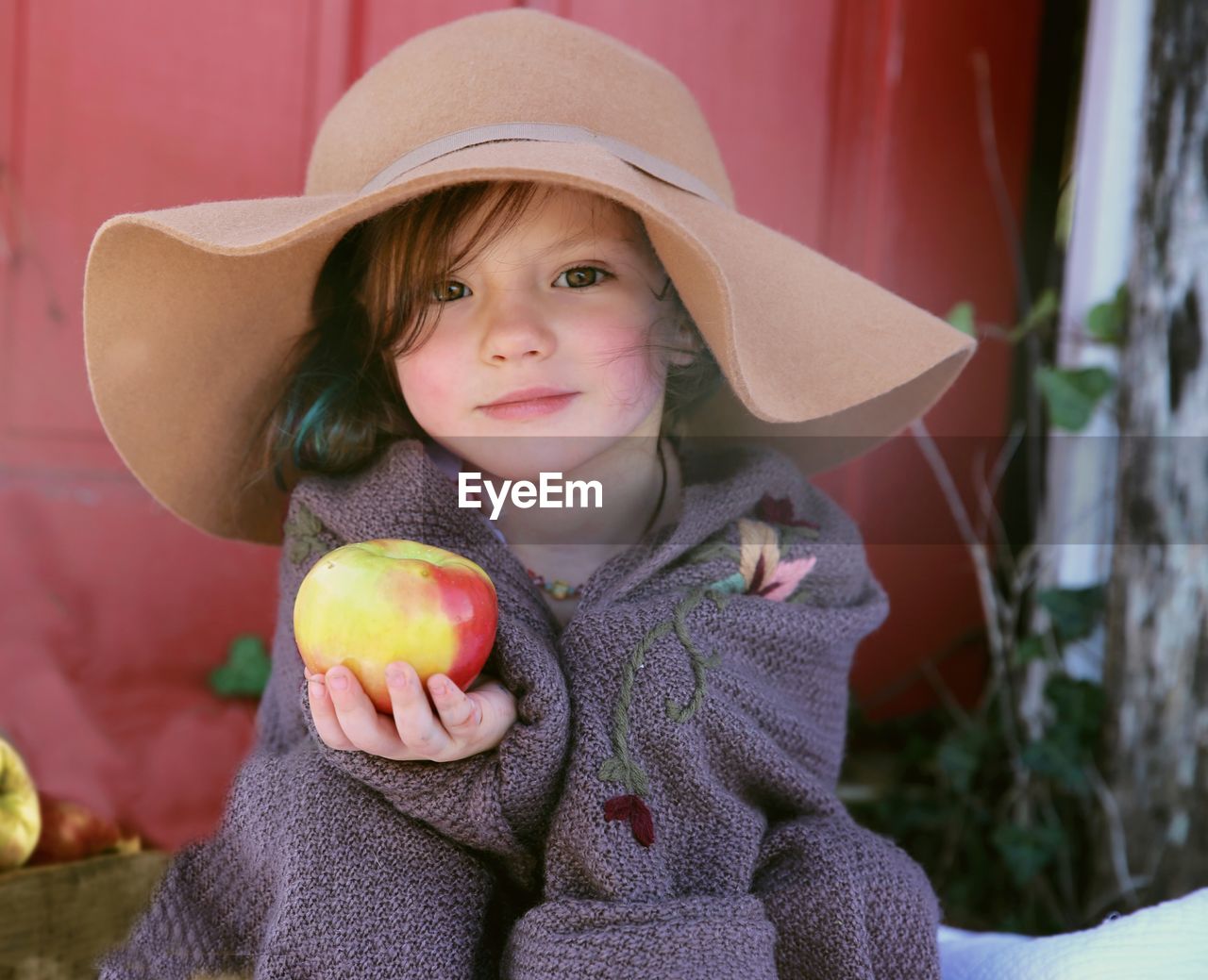 Portrait of cute girl holding apple while sitting outdoors