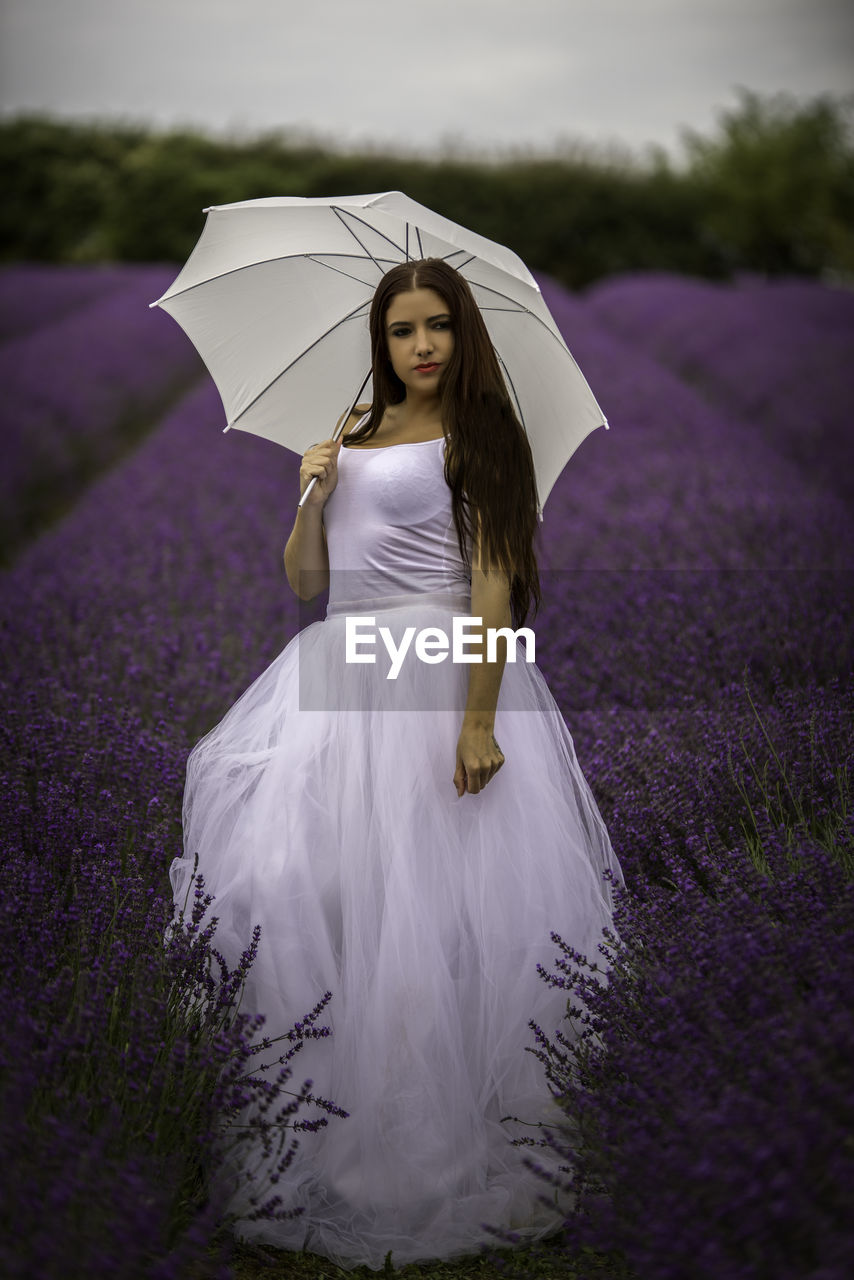 Portrait of young woman standing with umbrella on lavender field