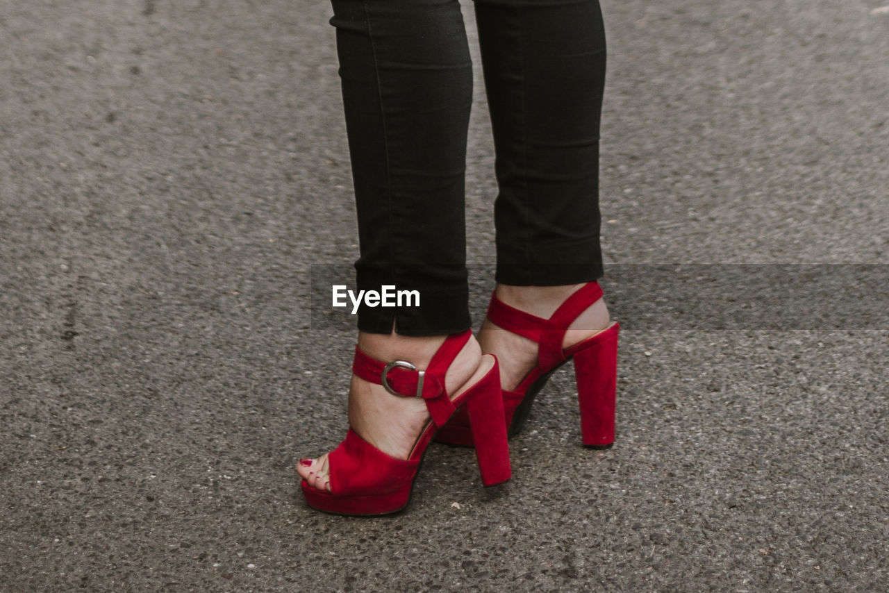 Low section of woman in red high heels standing on street