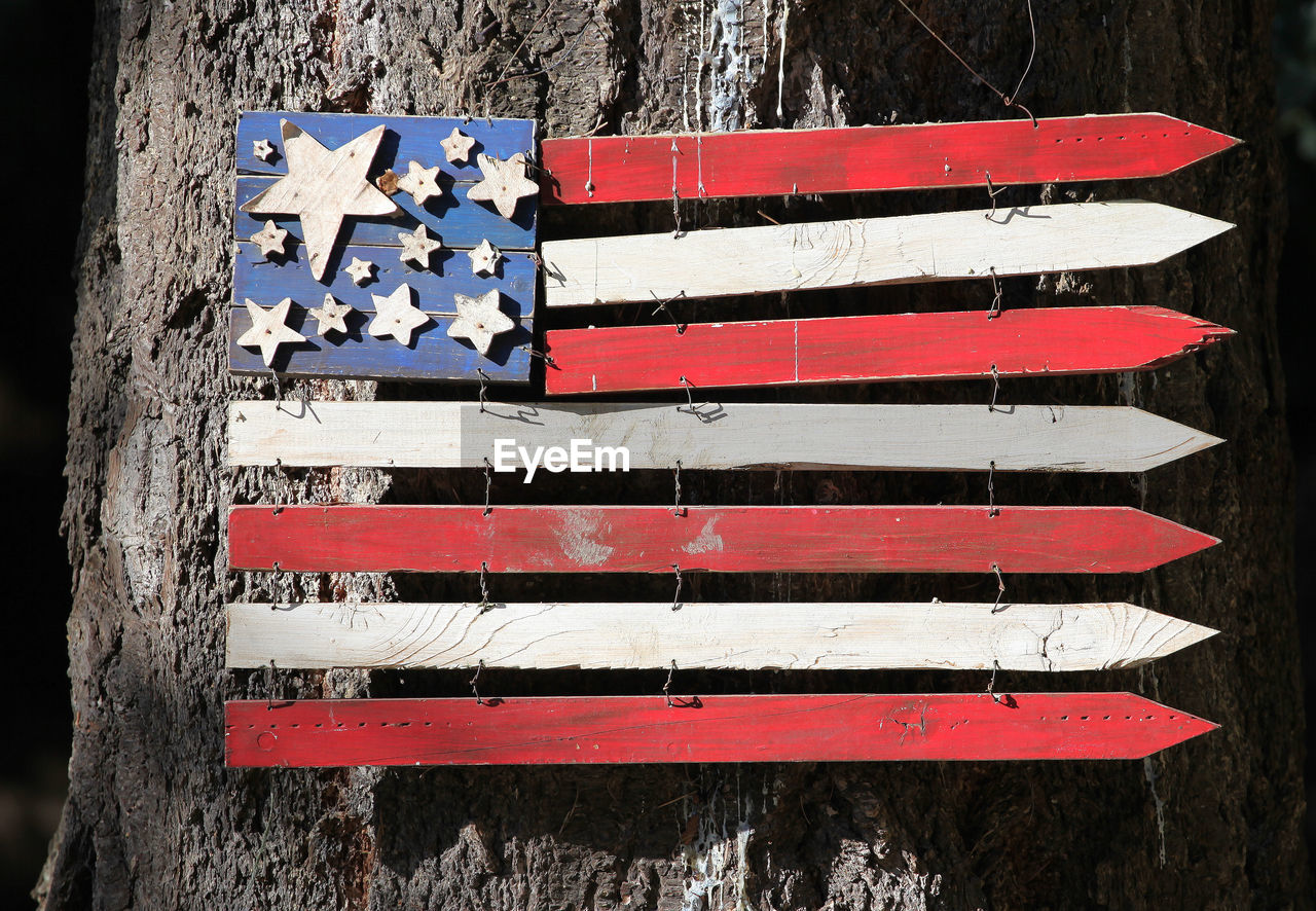 Usa wooden flag posted on a tree outdoors.