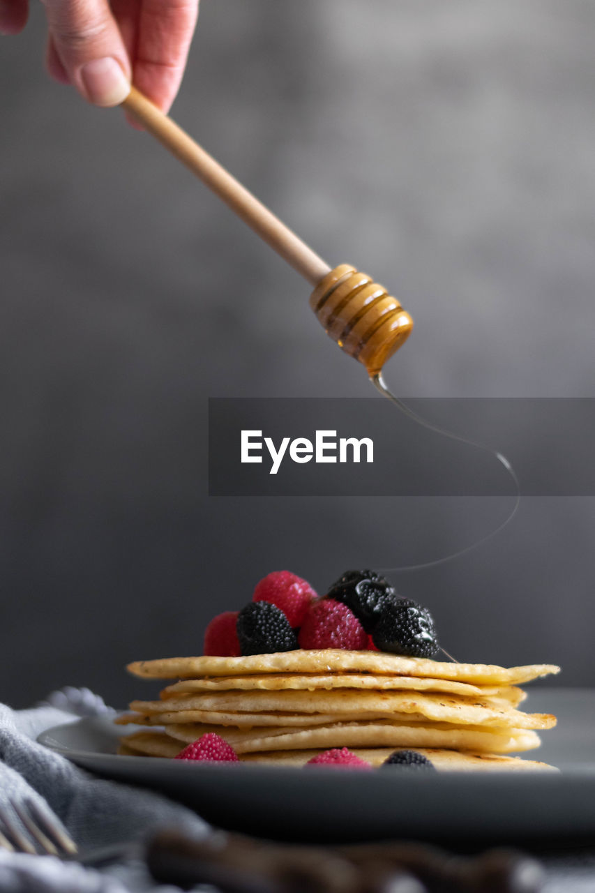 Pouring raw honey over homemade crepes on table, dark food photography