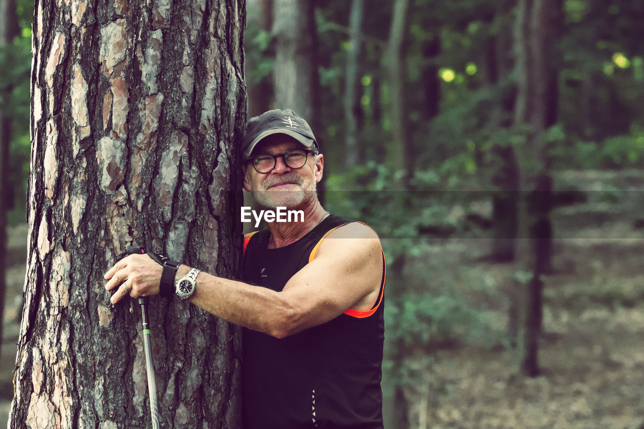 Portrait of a man standing and smiling by tree trunk in forest