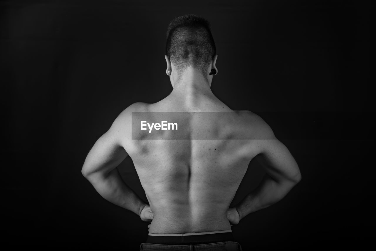 Rear view of shirtless man showing muscles against black background