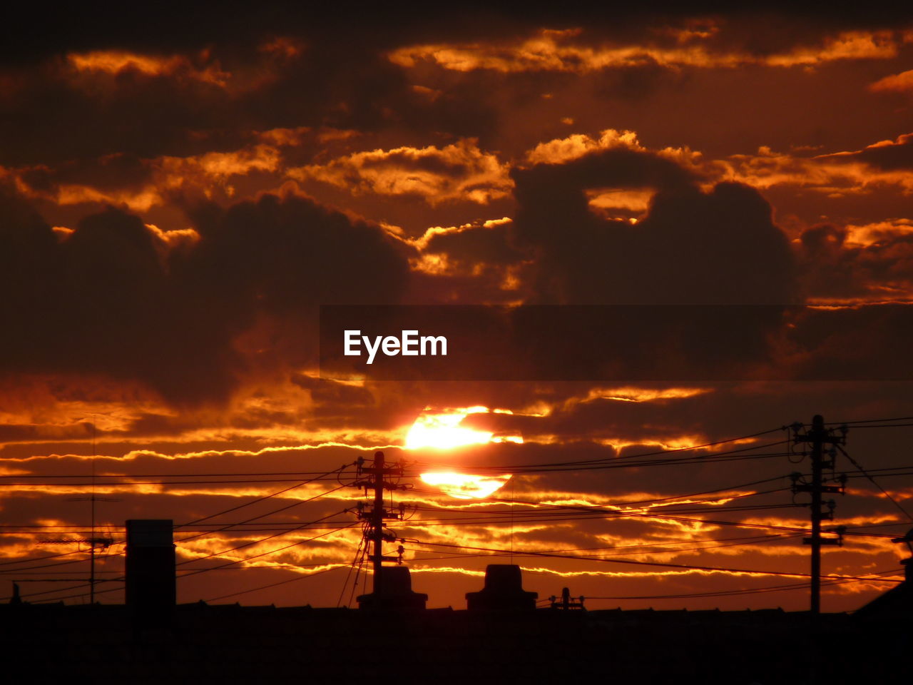 Silhouette electricity pylons against orange sunset sky