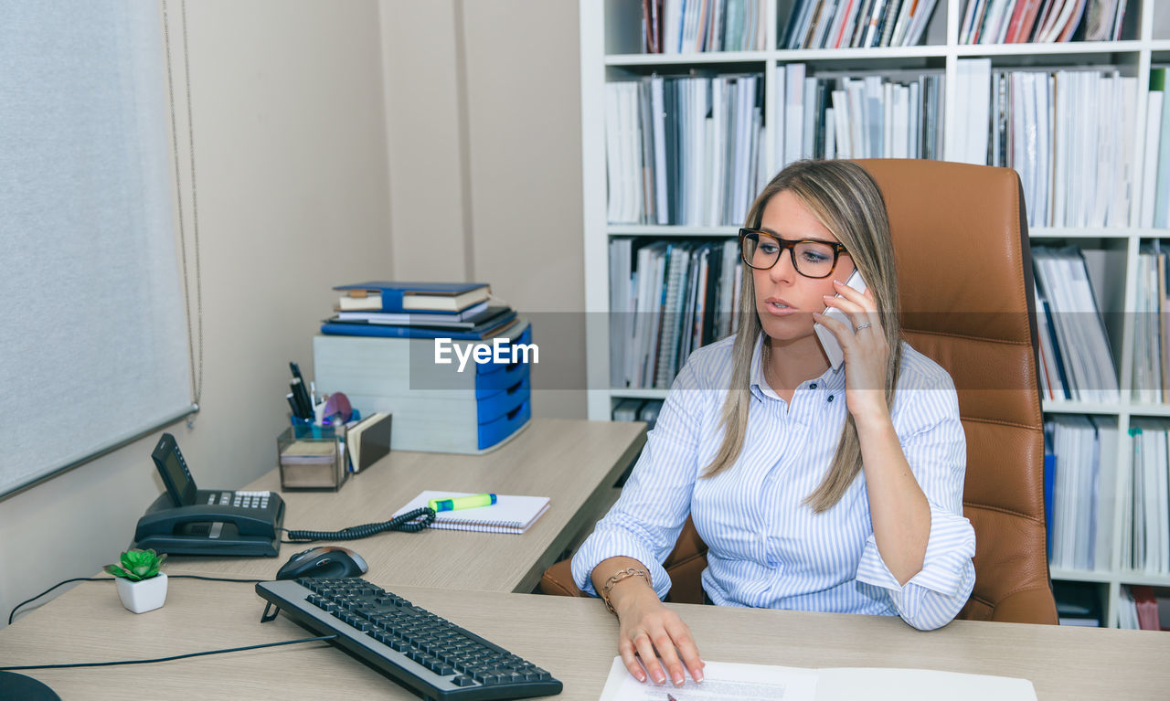 Businesswoman answering smart phone while working in office