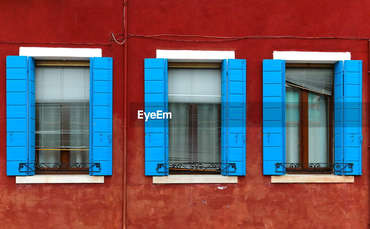 BLUE WINDOW OF BUILDING WITH RED CLOSED SHUTTER