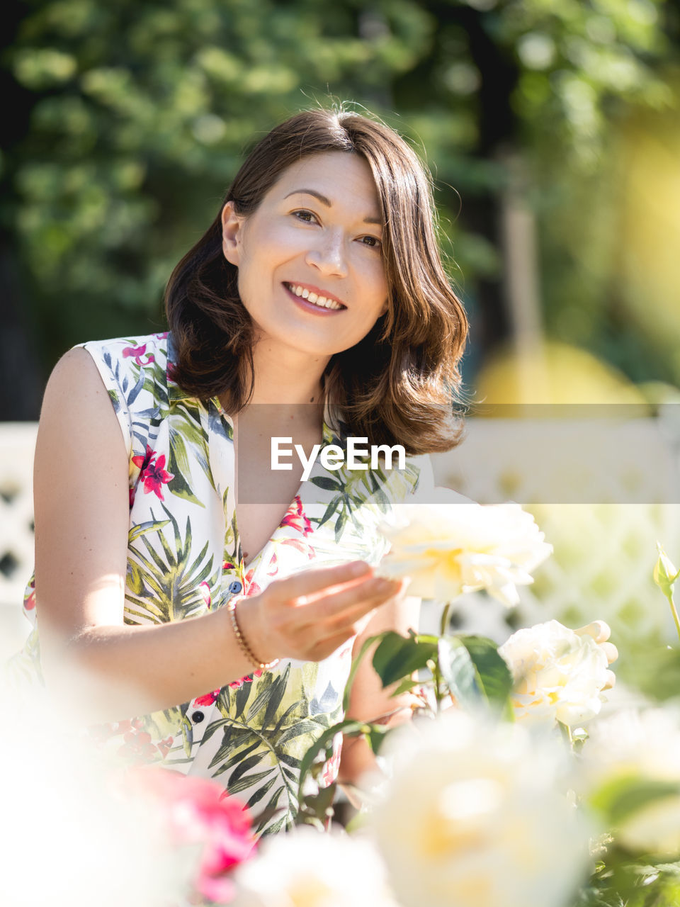 Caucasian woman is admiring of blooming roses in public park. summer vibes. tropical plants