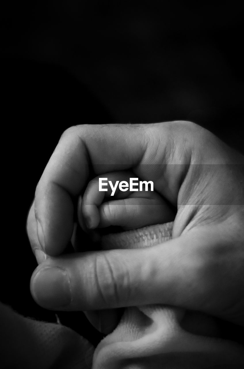 Cropped image of father holding son hand against black background