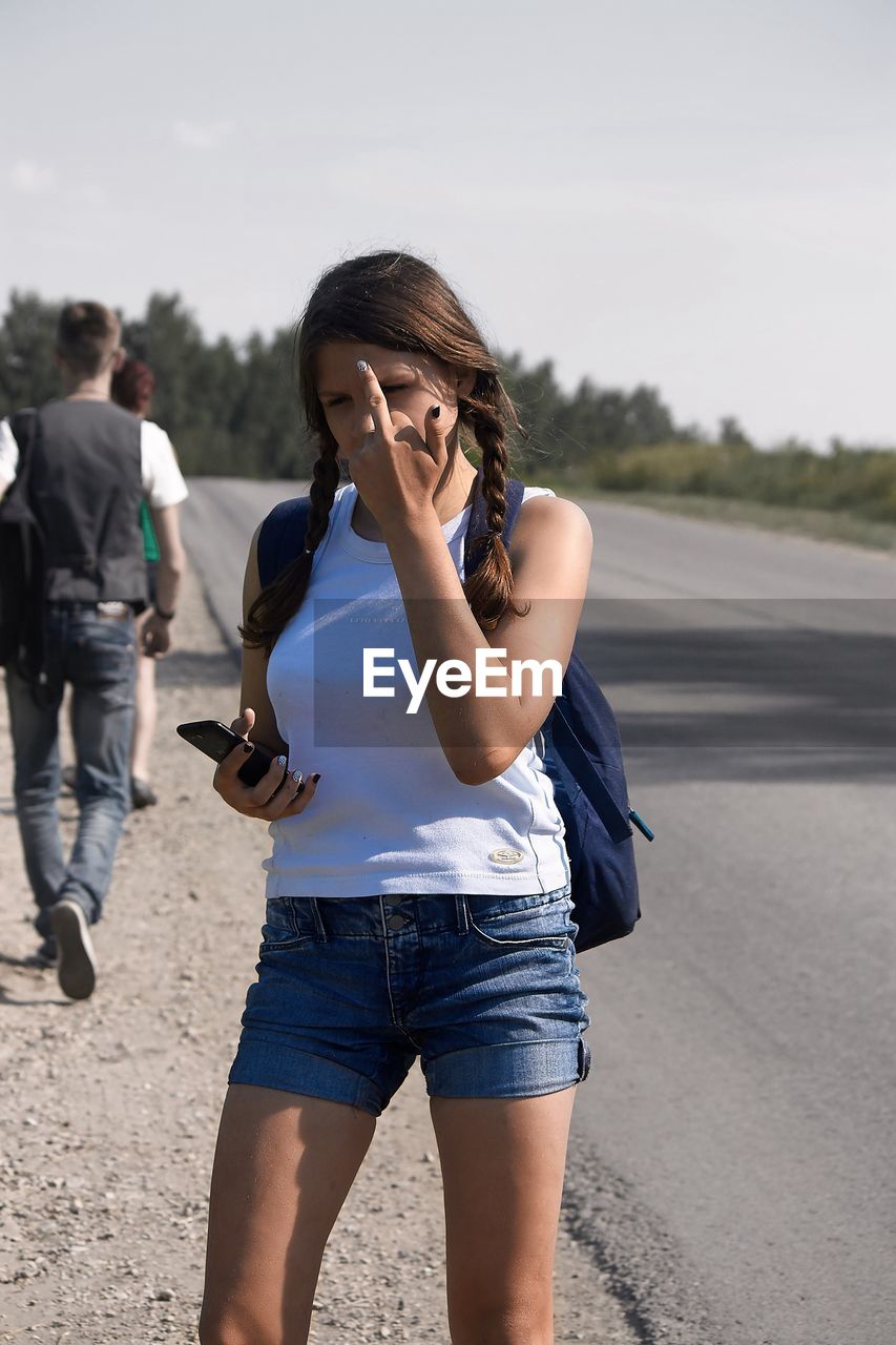 FULL LENGTH OF YOUNG WOMAN USING MOBILE PHONE AGAINST SKY