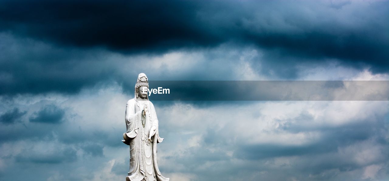 Low angle view buddha statue against storm clouds 