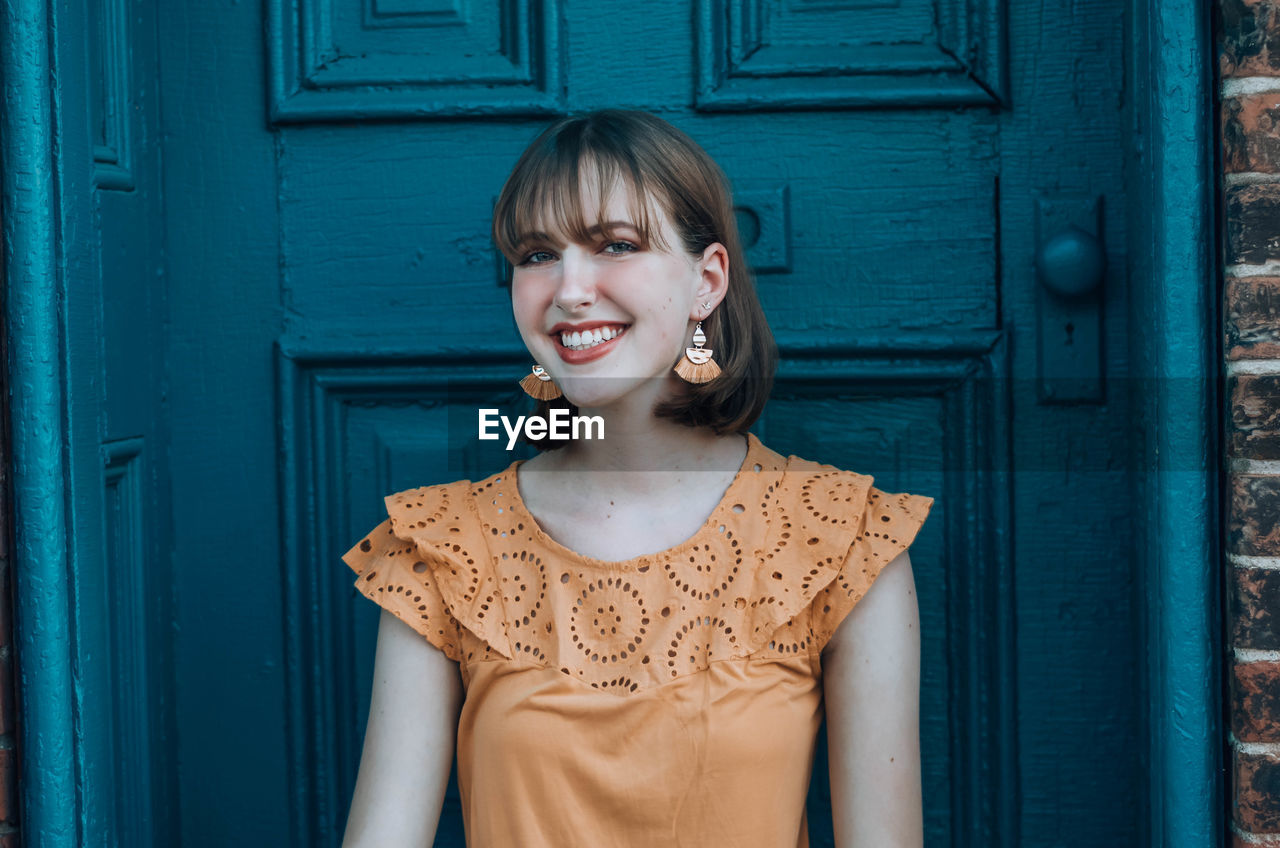 Portrait of smiling young woman sitting against door