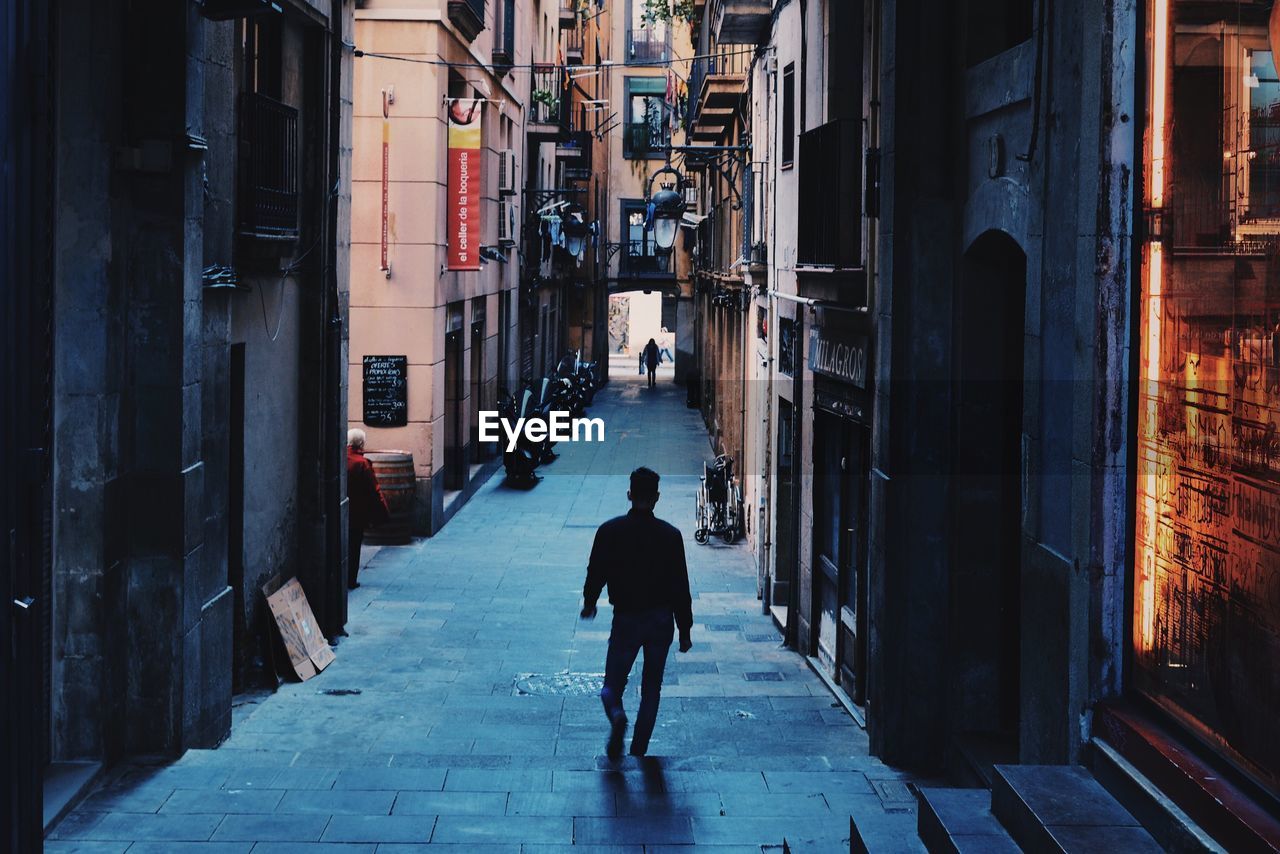 FULL LENGTH REAR VIEW OF A MAN WALKING ON NARROW STREET